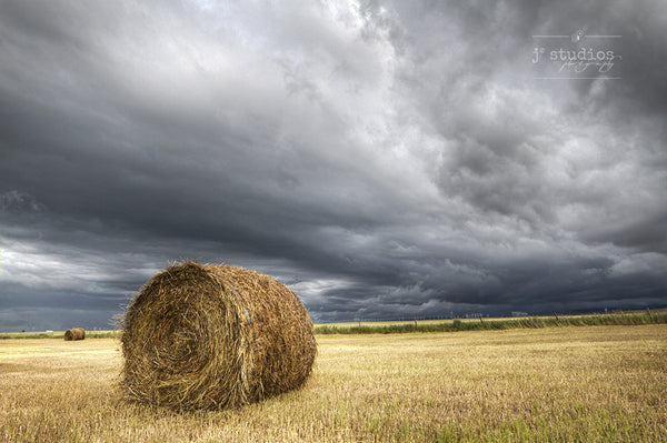 Dramatic image of a hay bale in farmer's field bracing itself for the incoming storm.