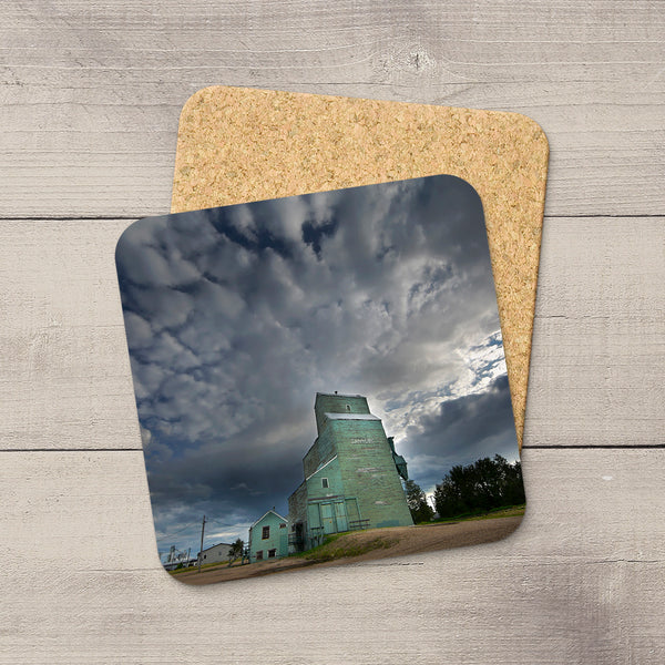 Square coaster with a glossy grain elevator photo, rounded corners, and a non-slip cork base on a wooden background.
