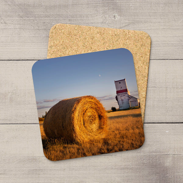 Square coaster with a cork base and glossy prairie hay bale and grain elevator print, 3.75 inches, on a wood background.
