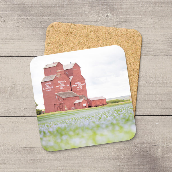 Square coaster with a red grain elevator photo, glossy finish, and protective cork backing on a wooden surface.