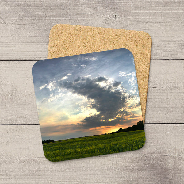 Square 3.75-inch coaster with a glossy prairie field sunset print and a protective cork bottom on a wood background.