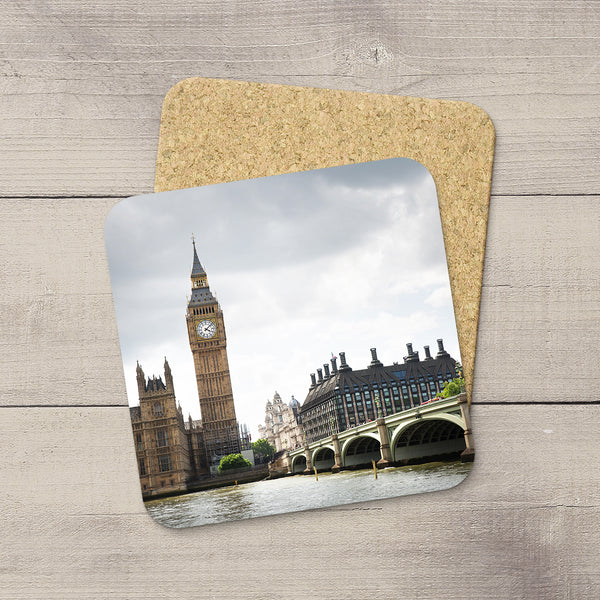 Two square cork coasters with rounded corners, one featuring a printed photograph of Big Ben and the Houses of Parliament in London, displayed on a light gray wood surface.