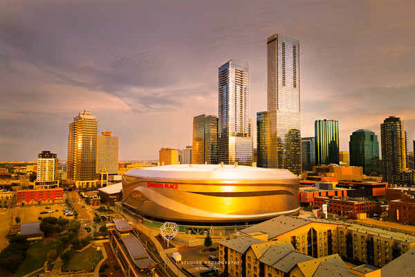Aerial view of Rogers Place arena in the foreground and the Edmonton skyline with skyscrapers under a warm sunset sky.