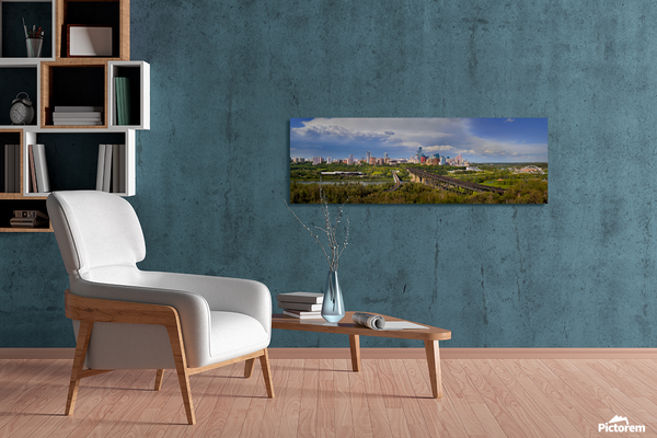 A panoramic canvas print of a city skyline over green parks, displayed on a textured teal wall in a modern living room setting with a white armchair and a wooden coffee table.