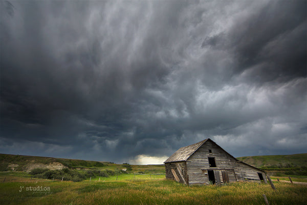 Dramatic image of the badlands in Sharples featuring a weathered barn standing steadfast against the incoming storm.  Storm photography of Alberta.