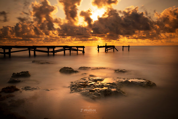 Image of the silky waters of the Caribbean Sea at sunrise in Playa del Carmen. Weathered and battered wooden pier frames this beautiful  photograph.