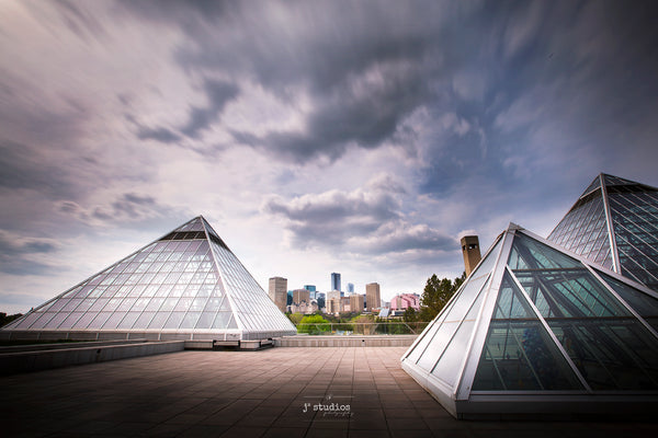 Moody image of trailing clouds over Muttart Conservatory. Three iconic glass pyramids framing the Edmonton City Skyline.