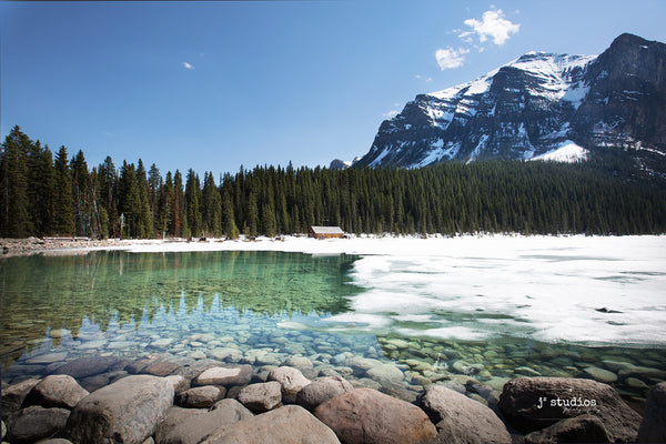 Image of the snow melting revealing the emerald green alpine waters of Lake Louise in Banff National Park. Alberta Photography.