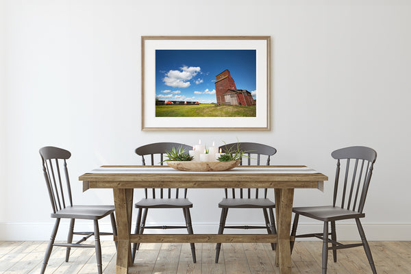Framed art print of train passing a grain elevator hanging on a dining room wall.
