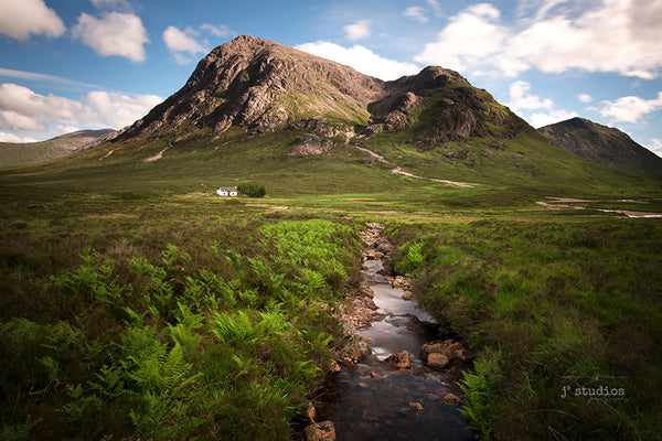 Image of creek with its water flowing peacefully towards an abandoned house by the mountains of Glen Coe in the Scottish Highlands. Landscape Travel Photography J2 Studios.